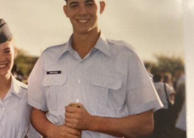 A young male military cadet in a light blue uniform and cap, smiling at the camera, holding a promotional product franchise yellow baton.