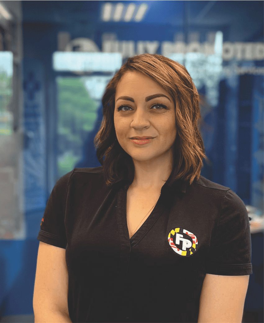 A woman with shoulder-length brown hair smiles gently, wearing a black polo shirt with an embroidered logo of a branded apparel franchise.