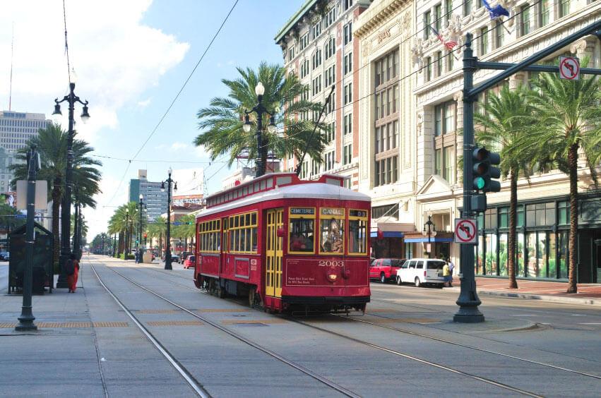 A red streetcar travels along a city street lined with palm trees and historic buildings on a sunny day. A red streetcar travels along a city street lined with palm trees and historic buildings on a sunny day.