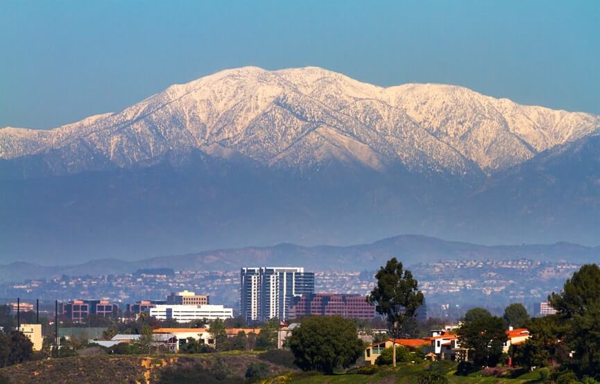 Snow-covered mountains with urban landscape and buildings in the foreground under a clear blue sky.