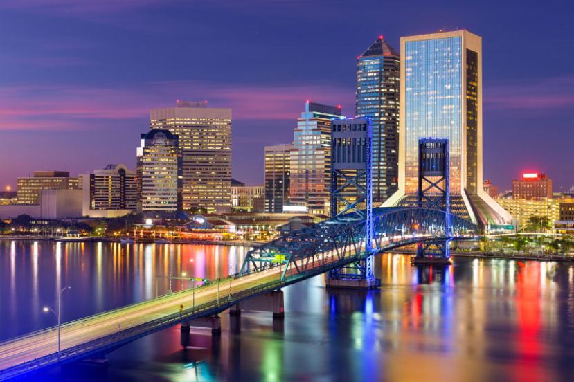 City skyline at dusk with illuminated skyscrapers and a lit-up bridge reflecting on the water. City skyline at dusk with illuminated skyscrapers and a lit-up bridge reflecting on the water.