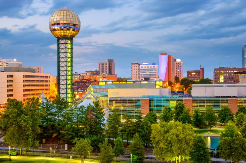 Skyline of Knoxville, Tennessee, featuring the Sunsphere, modern buildings, and trees under a cloudy sky.