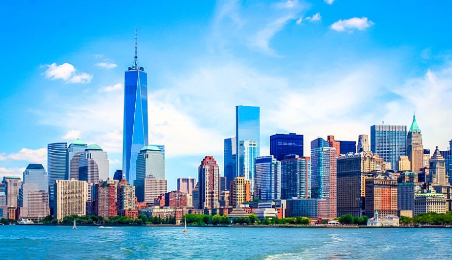 Skyline of New York City with a clear blue sky, featuring the One World Trade Center and various other skyscrapers across the waterfront.