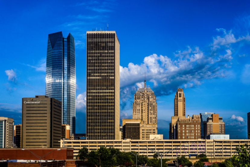 Skyline of a city with several tall buildings under a clear blue sky, featuring modern and historic architecture.